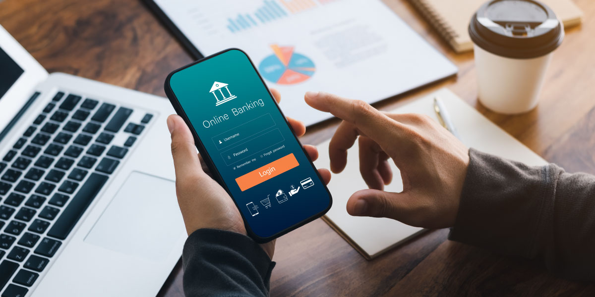 A person makes a payment using online banking on a phone while sitting in a coffee shop. The image illustrates digital payments and shopping through an online connection.